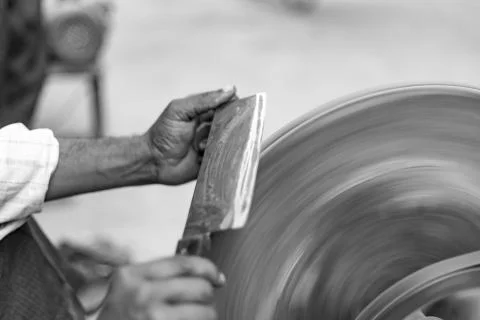 Hands of construction worker sharpens a knife on sanding machine Stock Photos