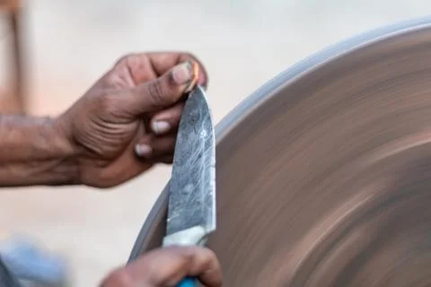Hands of construction worker sharpens a knife on sanding machine Stock Photos