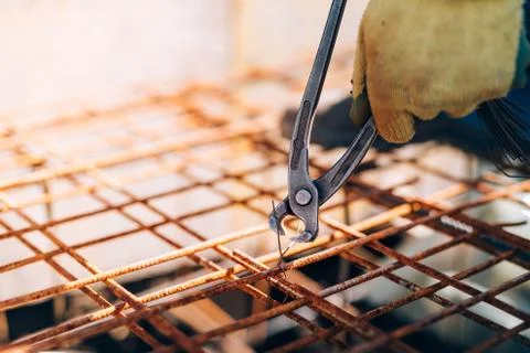 Hands of construction worker using pliers and securing steel bars with wire rod Stock Photos