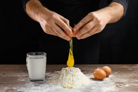 Hands of the cook close-up, breaks the egg into flour, a glass of fresh milk, Foto stock