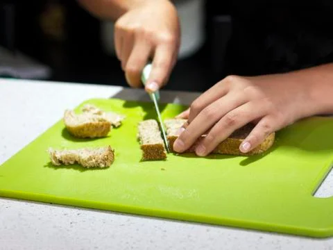 Hands of the cook cut bread with a knife on a green board Stock Photos