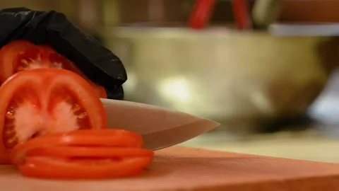 Hands of the cook in gloves. The chef cuts a tomato with a sharp knife. Stock Footage 234134894