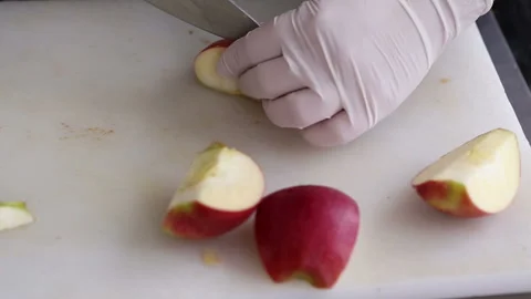 The hands of a cook with kitchen gloves cut a apple in slices with a knife Stock Footage 98644302