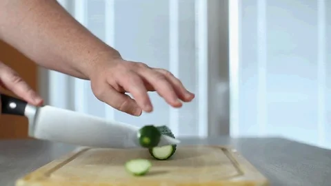 Hands of the cook knife big kitchen a fresh cucumber on a chopping board from a Stock Footage