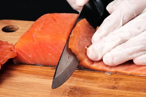 Hands cooks close-up. The chef cuts with a knife a red fish, smoked salmon on a Stock Photos