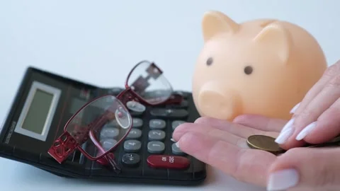 Hands counting coins next to calculator with glasses and piggy bank Stock Footage 290882913