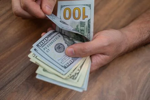 Hands counting US dollar banknotes on a wooden surface. Cash handling and Stock Photos
