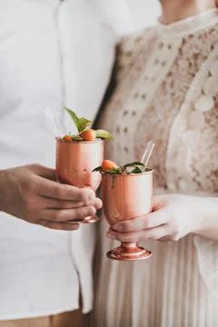 Hands of couple clinking brass goblets with ice citrus cocktail Stock Photos
