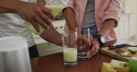 Hands of couple in kitchen preparing smoothie, pouring it into glass Vídeo Stock 340256339