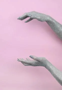 Hands covered in glitter reaching out against a soft pink backdrop. Stock Photos