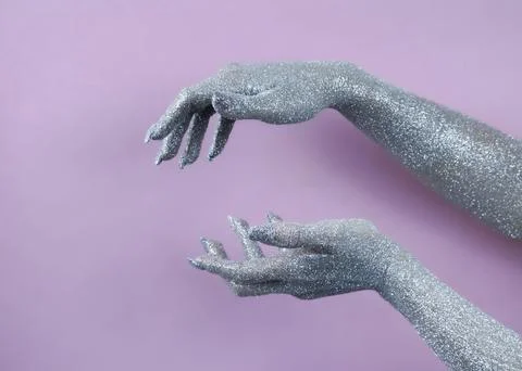 Hands covered in silver glitter creating an artistic pose against a pink ba.. Stock Photos