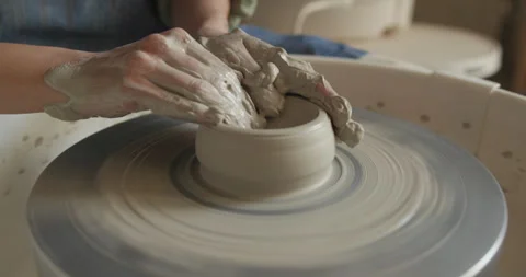 Hands covered in wet clay shape a spinning ceramic piece on a pottery wheel. The Stock Footage 302554671