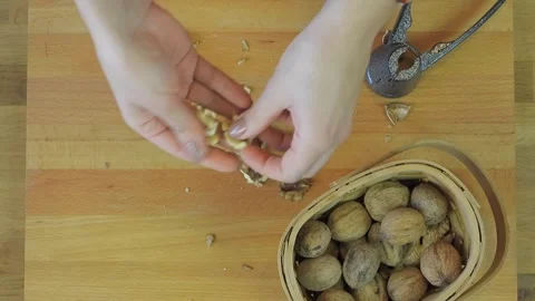 Hands crack fresh walnuts with a nutcracker on a wooden kitchen - Walnut Halves Stock Footage 339967112