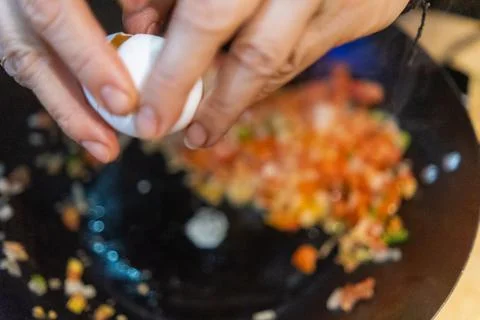 Hands cracking egg into frying pan with pico de gallo Foto stock