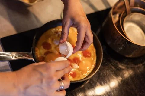 Hands cracking egg into frying pan with beaten eggs and yolk Stock Photos