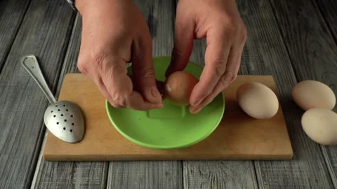 Hands cracking an egg into a green bowl using a slotted spoon on a wooden Stock Footage 333924855
