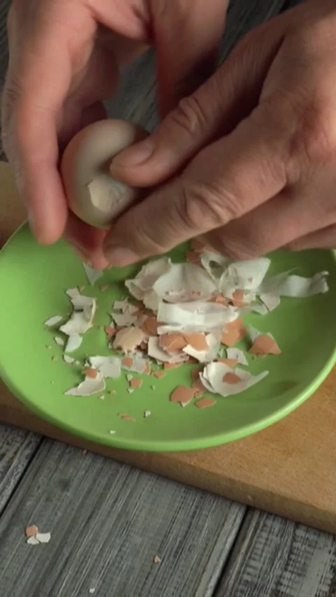 Hands cracking an egg over a green plate filled with broken eggshells on a Stock Footage 339030532