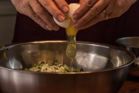 Hands cracking an egg over shredded zucchini in a bowl Stock Photos
