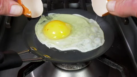 Hands cracking an egg into a very small frying pan. Video stock 141790976