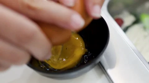 Hands Cracking a Fresh Raw Egg into a Small Black Bowl Stock Footage 334314090