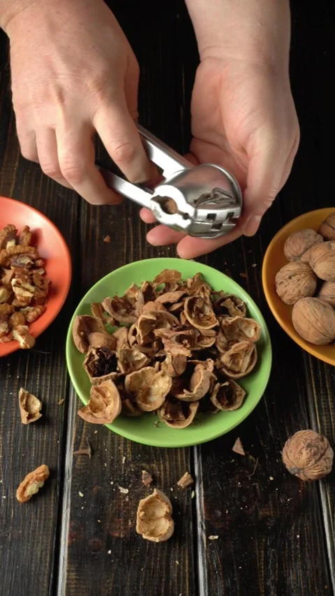 Hands cracking open walnut shells using a nutcracker, with broken shells and Stock Footage 328405575