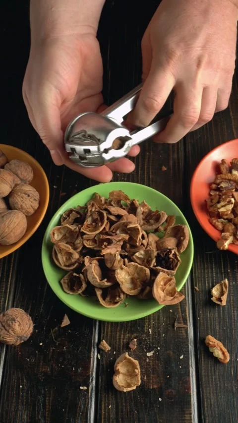Hands cracking open walnut shells with a nutcracker, revealing the nut inside, 스톡 동영상 335940472