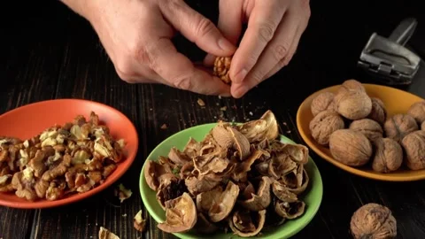 Hands cracking open walnuts, separating shells from nuts, with bowls of nuts and Stock Footage 328302023
