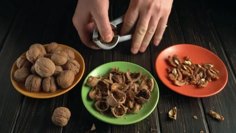 Hands cracking open walnuts using a nutcracker, with shells and nuts arranged on Video stock 335406967