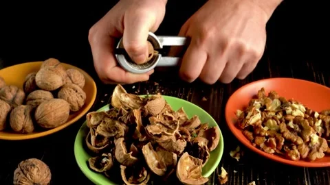 Hands cracking open walnuts using a nutcracker, with shells and nuts arranged on Video stock 335659112