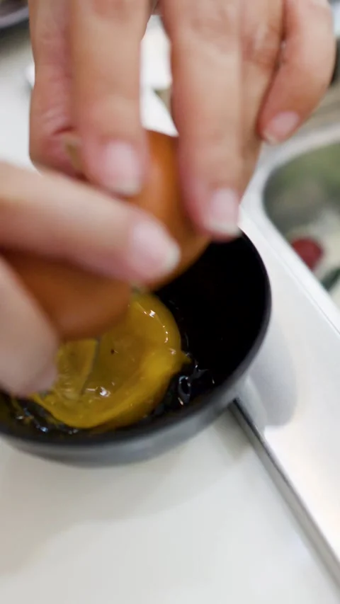 Hands Cracking a Raw Egg into a Small Black Bowl Stock Footage 334092923