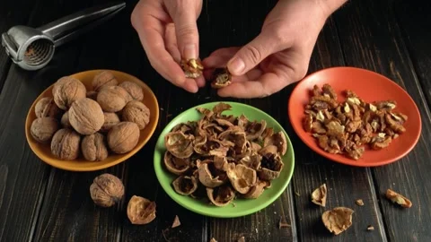 Hands cracking walnuts and separating shells from nuts on a wooden table with Stock Footage 335720239