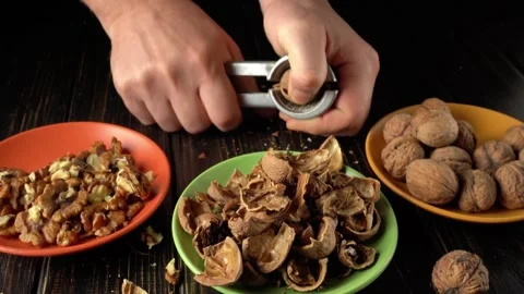 Hands cracking walnuts with a nutcracker, revealing the nut inside, surrounded Video stock 328159761