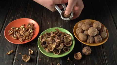 Hands cracking walnuts using a nutcracker, with broken shells and shelled nuts Video stock 328362815