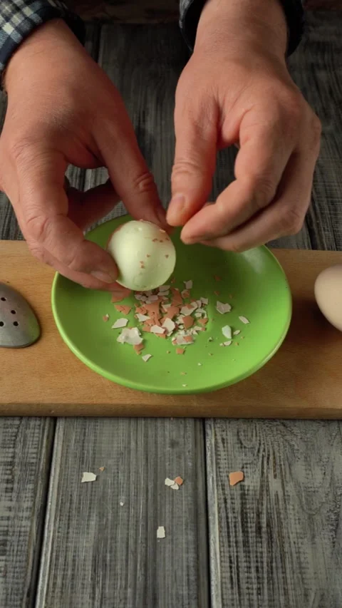 Hands cracking a white egg over a green bowl, revealing shell fragments and Stock Footage 333707223