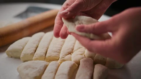 Hands craft dough logs with care on flour-dusted counter Stock Footage 336096477
