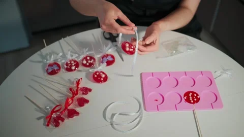 Hands craft red lollipops with white patterns, using tools Vidéo 336054670