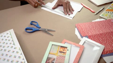 Hands Crafting with Patterned Scrapbook Paper and Tools on Tabletop Workspace Stock Footage 345617038