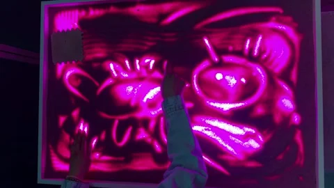 Hands creating glowing sand art on neon light table Stock Footage 336542430