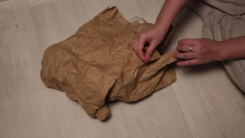 Hands crumpling brown paper bag on wooden floor, preparing for recycling or Stock Footage 339176096