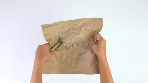 Hands crumpling brown paper with sorry word isolated on a white background. Stock Footage 114558181
