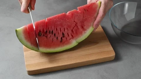 Hands cut watermelon wedge into even portions beside glass bowl for easy summer Stockbeeldmateriaal 345792878