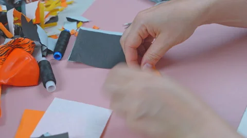 Hands cutting and arranging orange and black fabric pieces on a pink craft .. Vídeo Stock 346800441