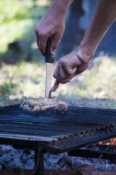 Hands cutting chicken while it is cooking on the grill during a barbecue. Stock Photos