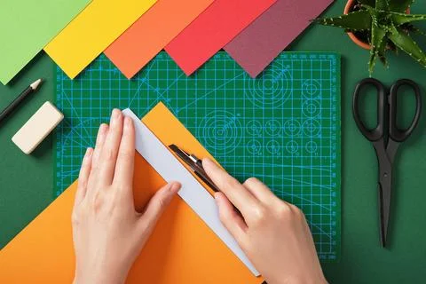 Hands cutting colored paper with utility knife on green cutting mat in top vi Stock Photos