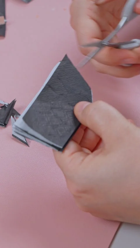 Hands cutting dark fabric into small pieces with scissors on a pink table 스톡 동영상 346982600