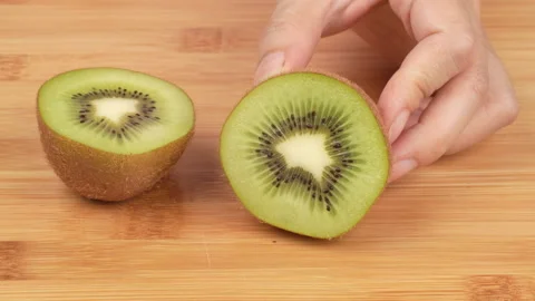 Hands Cutting Fresh Kiwi Fruit in Half with Knife on Wooden Board Stock Footage 319911072