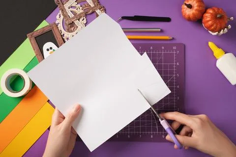 Hands cutting ghost shape from white paper with scissors during Halloween cra Stock Photos