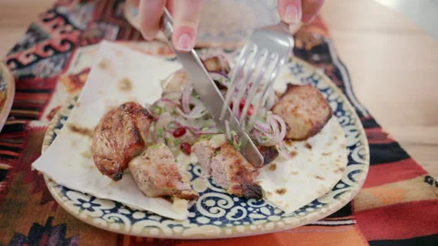 Hands cutting grilled meat with fork and knife on a plate with flatbread and Stock Footage 332607687