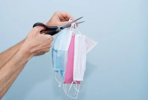 Hands cutting a group of masks with scissors on a blue background. Stock Photos