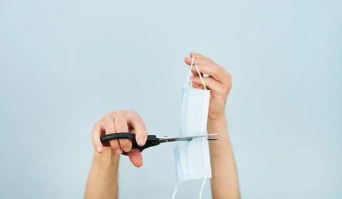 Hands cutting a mask with scissors on blue background. Copy space. Stock Photos
